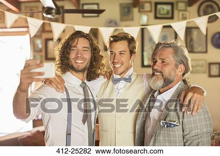 Stock Image - "Best man, bridegroom and father taking selfie in domestic room". Fotosearch