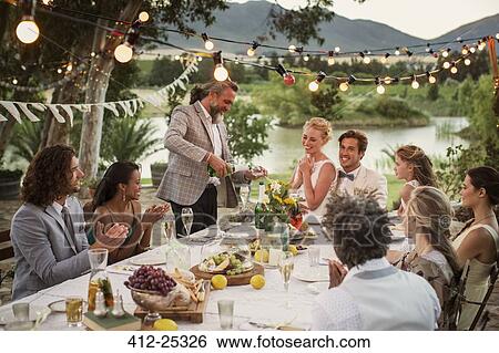 Stock Photograph - Best man pouring champagne into flutes during wedding reception in domestic garden. Fotosearch