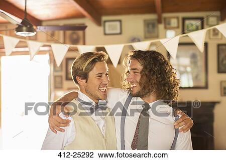 Stock Image - Bridegroom and best man embracing in domestic room. Fotosearch