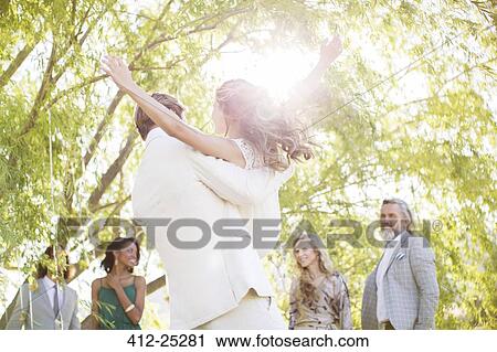 Stock Image - Bridegroom picking bridesmaid up at wedding reception in domestic garden. Fotosearch