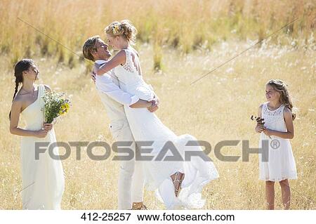 "Bridesmaid and bridesmaid watching and laughing, Young couple embracing in meadow" View Large Photo Image Stock Photo - "Bridesmaid and bridesmaid watching and laughing, Young couple embracing in meadow". Fotosearch