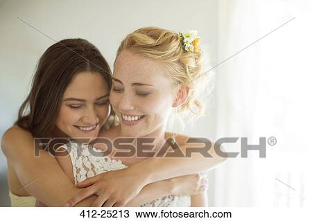 Stock Image - Bridesmaid embracing bride in bedroom. Fotosearch