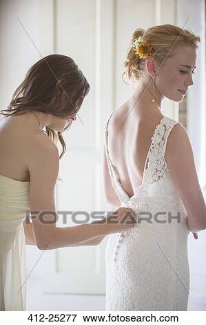 Stock Photo - Bridesmaid helping bride with dressing in domestic room. Fotosearch