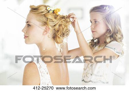 Stock Image - Bridesmaid helping bride with hairstyle in domestic room. Fotosearch