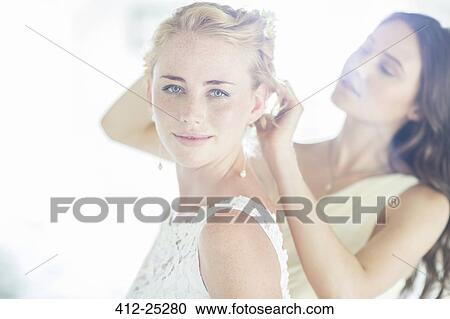 Stock Image - Bridesmaid helping bride with hairstyle in domestic room. Fotosearch