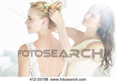 Stock Photo - Bridesmaid helping bride with hairstyle in garden. Fotosearch