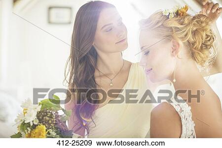 Stock Photo - Bridesmaid helping bride with hairstyle in bedroom. Fotosearch
