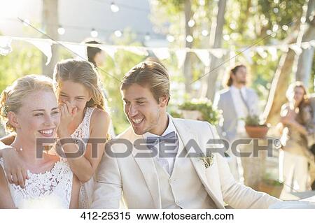 Stock Photography - Bridesmaid whispering to bride's ear during wedding reception in domestic garden. Fotosearch