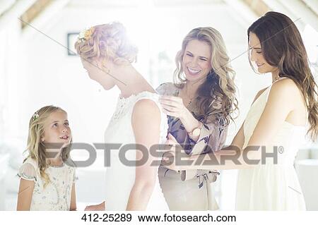 Matron of honor and bridesmaid helping bride with dressing in domestic room View Large Photo Image Stock Photo - Matron of honor and bridesmaid helping bride with dressing in domestic room. Fotosearch