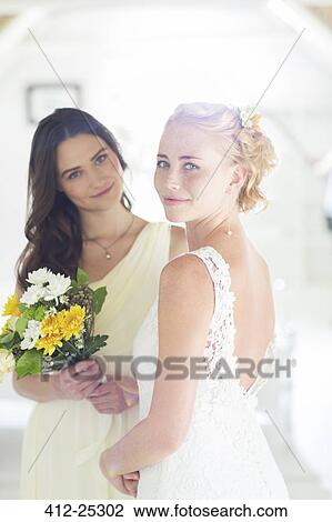 Stock Image - Portrait of bride and bridesmaid with bouquet of flowers in domestic room. Fotosearch