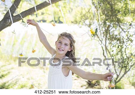 Stock Image - Smiling bridesmaid playing with decorations in domestic garden during wedding reception. Fotosearch