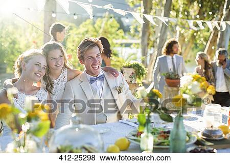 Stock Photo - Young couple and bridesmaid during wedding reception in domestic garden. Fotosearch