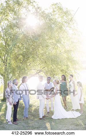 Stock Photograph - Young couple and guests during wedding ceremony in domestic garden. Fotosearch