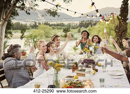 Stock Image - Young couple and guests toasting with champagne during wedding reception in domestic garden. Fotosearch