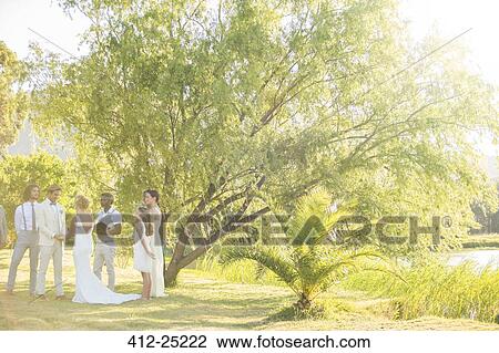 Young couple and their guests standing in garden attending wedding ceremony View Large Photo Image Stock Image - Young couple and their guests standing in garden attending wedding ceremony. Fotosearch