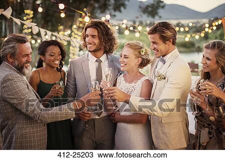 Stock Image - Young couple and their guests with champagne flutes during wedding reception in garden. Fotosearch