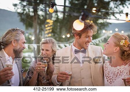 Stock Photo - Young couple and their guests with champagne flutes during wedding reception in garden. Fotosearch
