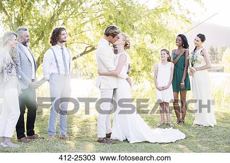 Stock Image - Young couple embracing and kissing during wedding ceremony in domestic garden. Fotosearch