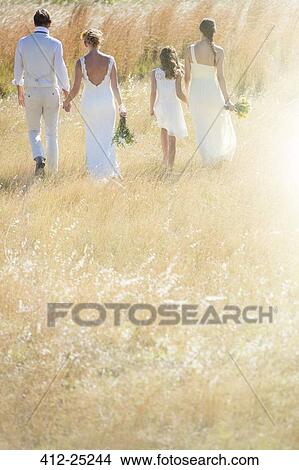 Picture - Young couple with bridesmaid and girl walking in meadow. Fotosearch
