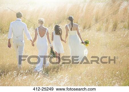 Stock Photo - Young couple with bridesmaid and girl walking in meadow. Fotosearch