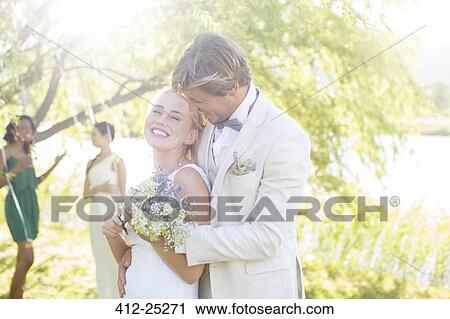 Stock Image - Young couple with bunch of flowers at wedding reception in domestic garden. Fotosearch
