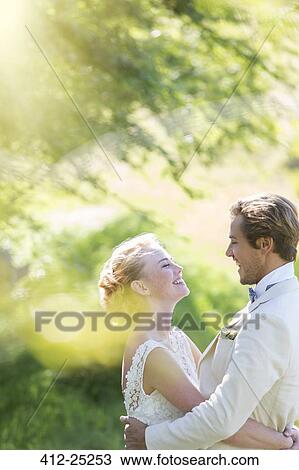 Stock Image - Young smiling couple embracing in domestic garden. Fotosearch