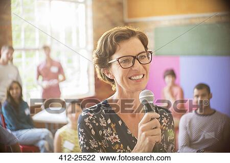 Stock Image - Audience behind smiling speaker with microphone at community center. Fotosearch