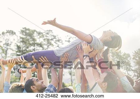 Stock Image - Carefree woman crowdsurfing supported by team. Fotosearch