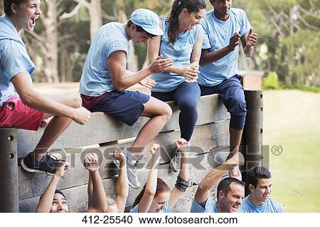 Stock Image - Cheering team at wall on boot camp obstacle course. Fotosearch