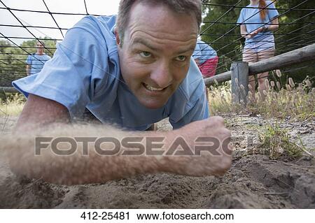Stock Image - Determined man crawling on boot camp obstacle course. Fotosearch