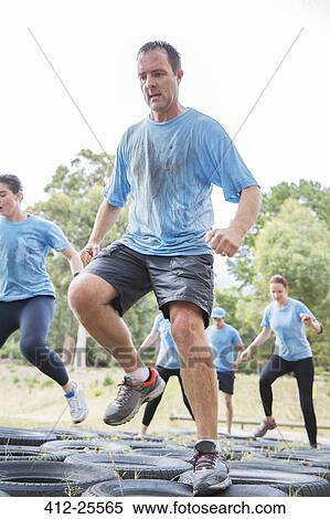 Stock Photography - Determined man jumping tires on boot camp obstacle course. Fotosearch