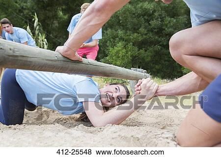 Teammate helping woman under log on boot camp obstacle course View Large Photo Image Stock Photo - Teammate helping woman under log on boot camp obstacle course. Fotosearch