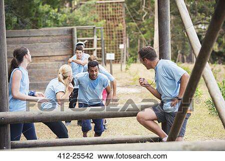 Stock Image - Teammates cheering man on boot camp obstacle course. Fotosearch