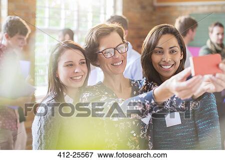 Stock Photo - Women taking selfie with camera phone in community center. Fotosearch