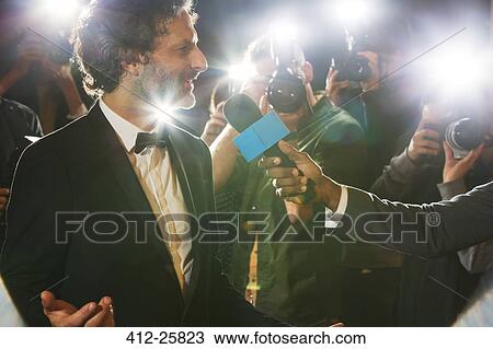 Stock Image - Celebrity being interviewed and photographed by paparazzi at event. Fotosearch