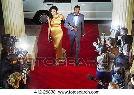 Stock Photo - Celebrity couple arriving at red carpet event and being photographed by paparazzi. Fotosearch