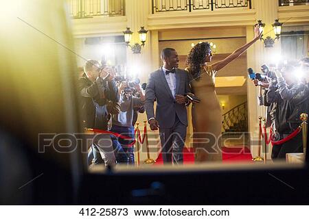 Stock Image - Celebrity couple leaving red carpet event and waving to paparazzi photographers. Fotosearch