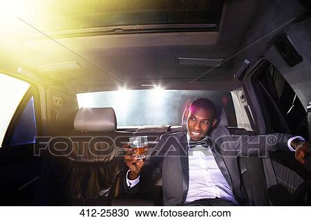 Stock Image - Celebrity drinking cocktail inside limousine outside event. Fotosearch