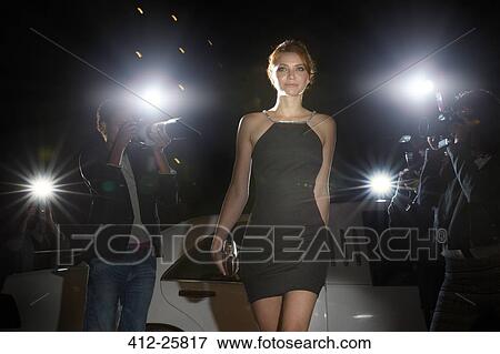 Stock Photo - Celebrity in black dress arriving at event and being photographed by paparazzi. Fotosearch