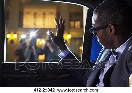Stock Image - Celebrity in limousine waving at paparazzi photographers. Fotosearch