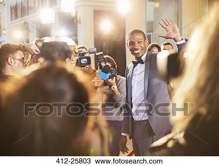 Stock Image - Celebrity waving for paparazzi with cameras at event. Fotosearch