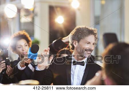 Stock Image - Celebrity waving to paparazzi at event. Fotosearch