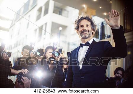 Stock Image - Celebrity waving to paparazzi photographers at event. Fotosearch