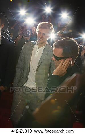 Stock Photo - Smiling celebrity arriving at red carpet event and being photographed by paparazzi. Fotosearch