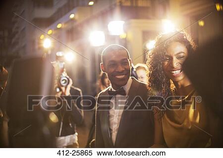 Stock Photography - Smiling celebrity couple being photographed by paparazzi at event. Fotosearch