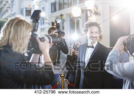 Smiling celebrity in tuxedo being photographed by paparazzi at red carpet event View Large Photo Image Stock Photograph - Smiling celebrity in tuxedo being photographed by paparazzi at red carpet event. Fotosearch