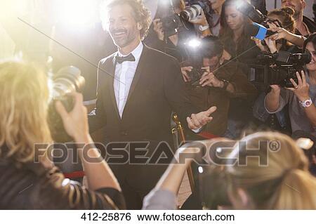 Stock Photograph - Smiling celebrity posing for paparazzi photographers at event. Fotosearch