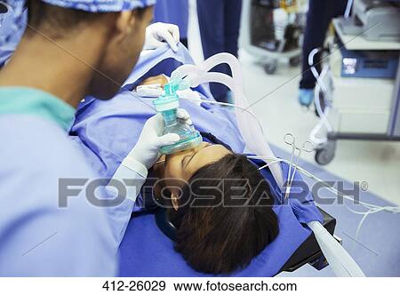 Stock Photo - Anesthesiologist holding oxygen mask over patient’s face in operating room. Fotosearch