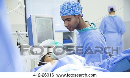 Stock Photograph - Anesthesiologist holding oxygen mask over patient’s face in operating room. Fotosearch