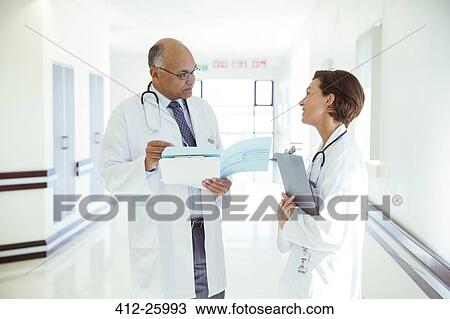 Doctors discussing medical record in hospital corridor View Large Photo Image Stock Image - Doctors discussing medical record in hospital corridor. Fotosearch